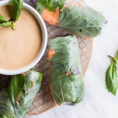 A plate with Thai spring rolls arranged around a bowl of peanut sauce.