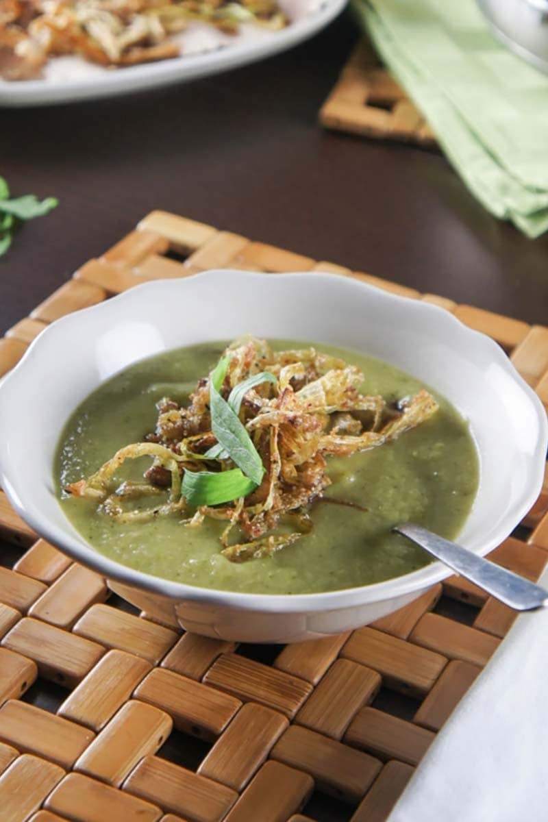 A white bowl with broccoli leek soup topped with crispy fried leeks.