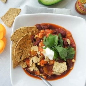 A bowl of eggplant chili shown garnished with chips and cilantro.