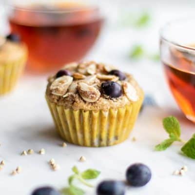 Two buckwheat muffins sitting next to mugs of tea.