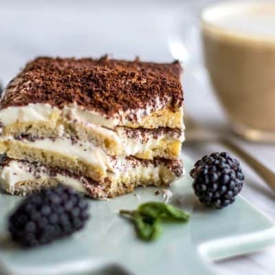 A slice of greek yogurt tiramisu, with a bite taken out of the corner revealing the layers of lady fingers and creamy yogurt filling.