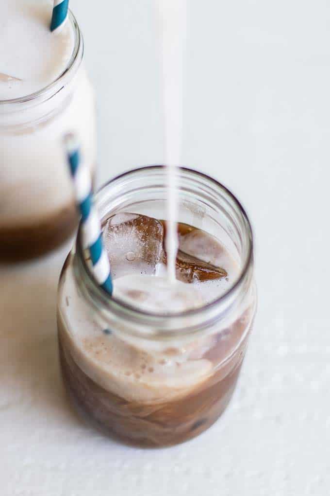 A mason jar with salted caramel mocha coffee concentrate, with almond milk being poured in.