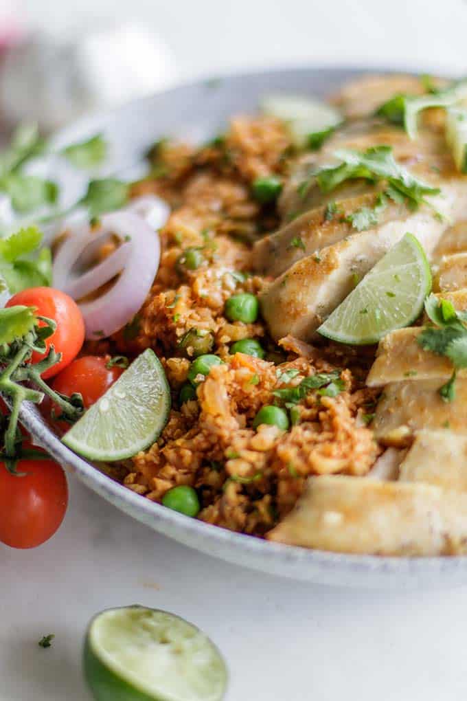 A bowl filled with whole30 mexican rice and chicken, garnished with limes and cilantro.