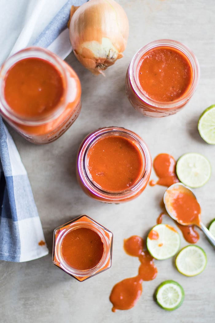 Jars of gluten free enchilada sauce surrounded by onions and limes.