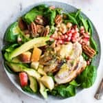 A vibrant green spinach salad topped with chicken, apples, pomegranate, pecans and avocado.