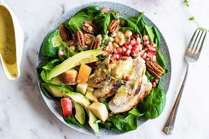 A vibrant green spinach salad topped with chicken, apples, pomegranate, pecans and avocado.