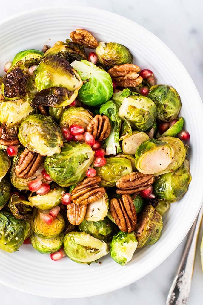 A close up of a serving bowl filled with crispy roasted brussels sprouts.