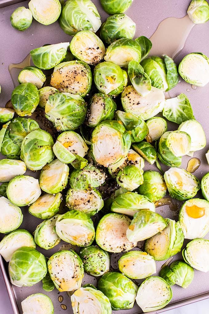 A baking tray with brussels sprouts cut in half, drizzled with honey and olive oil.