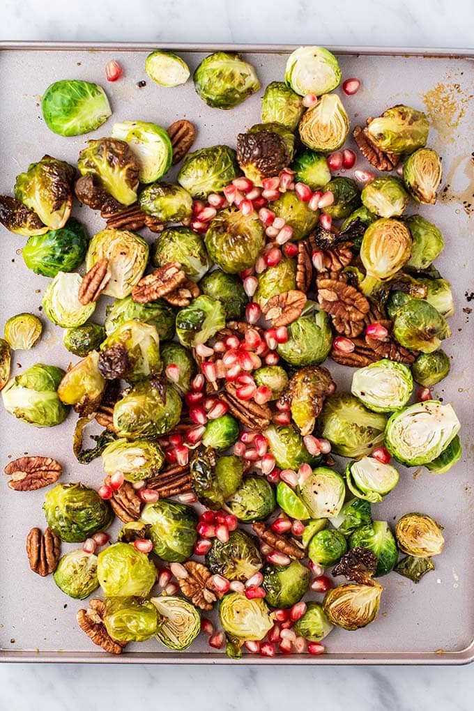 A baking sheet covered in crispy roasted brussels sprouts, topped with pecans and pomegranate.