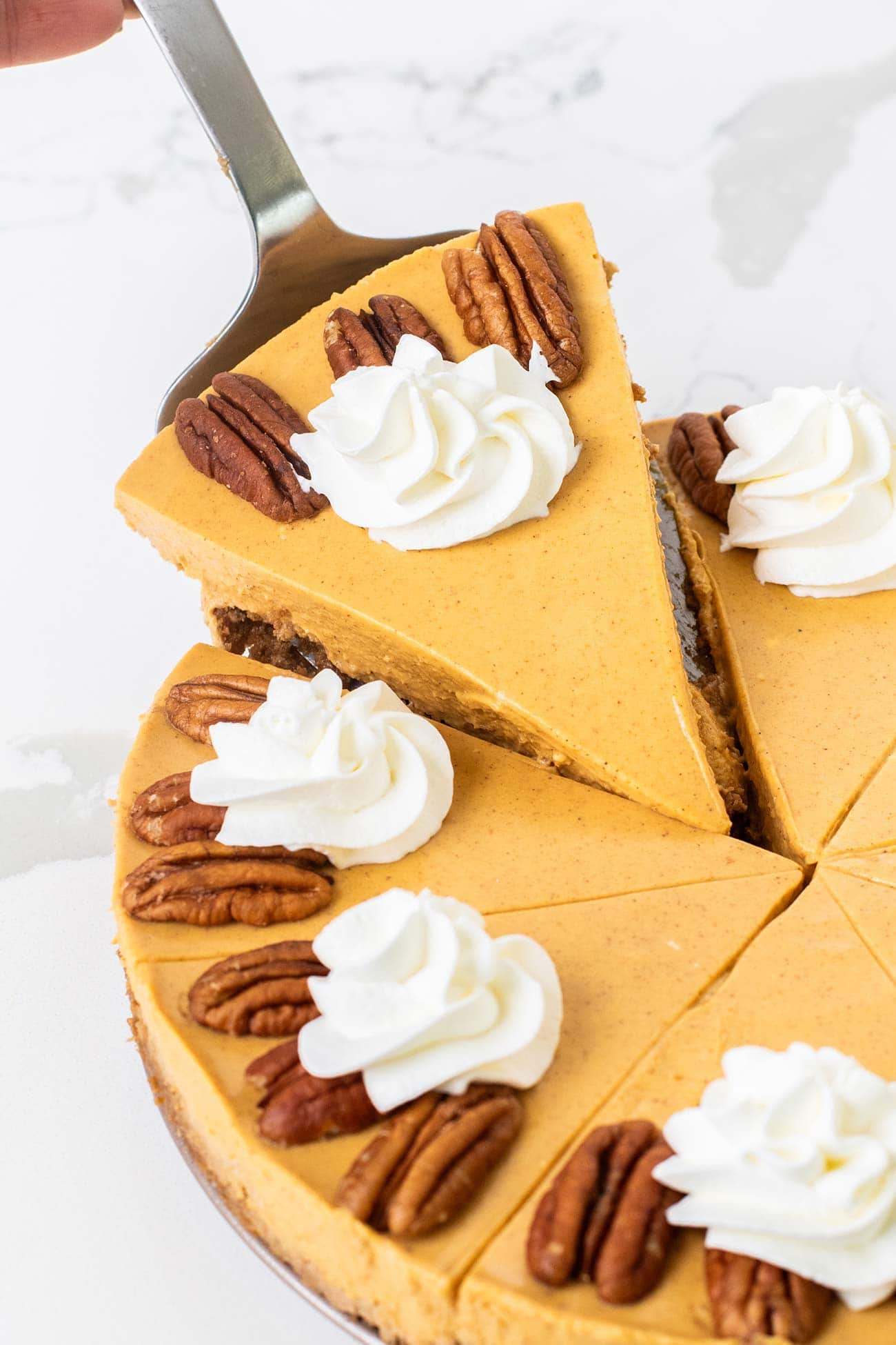A slice of Greek yogurt pumpkin cheesecake being taken out of a whole cake.
