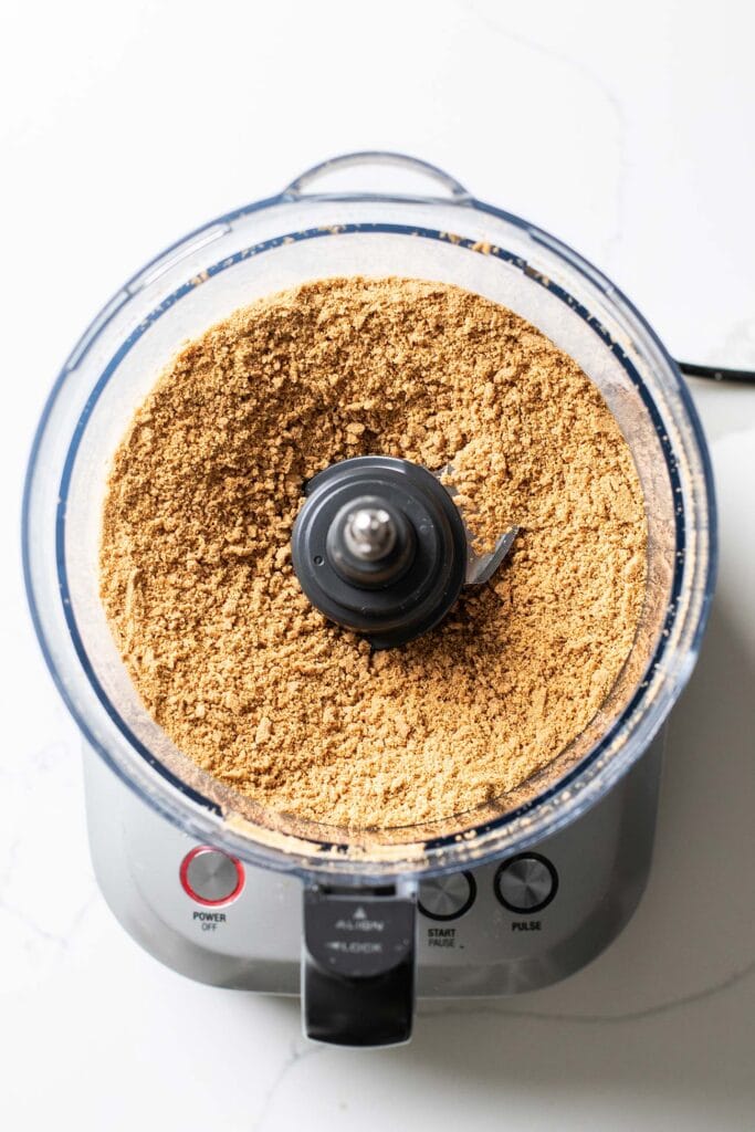 Gluten-free graham crackers in a food processor shown processed into a crumb texture.