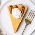 A slice of Greek yogurt pumpkin cheesecake shown garnished with pecans and whipped cream.