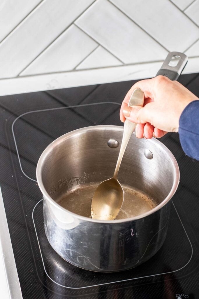 A saucepan with gelatin and water being stirred while heated to melt.