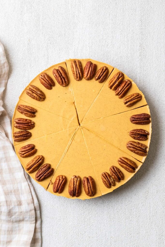 A pumpkin cheesecake cut into slices and garnished with pecan halves.