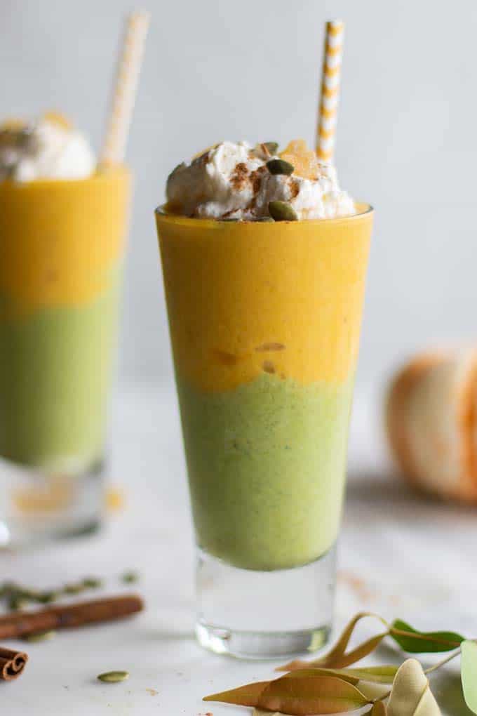 Two green pumpkin pie smoothies topped with whipped cream.
