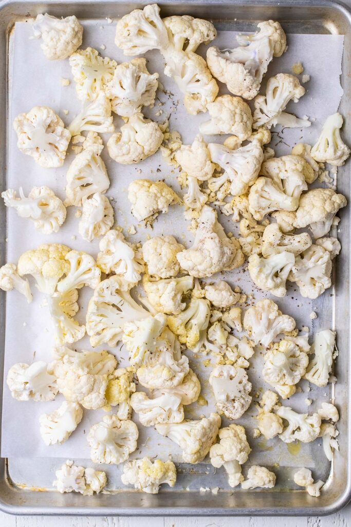 Cauliflower florets on a baking sheet drizzled with olive oil and spices.