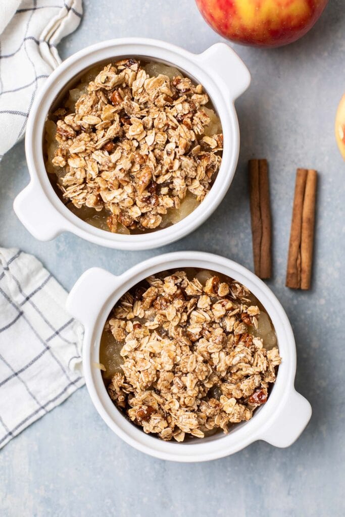 Two ramekins of applesauce shown topped with an oatmeal crumble.