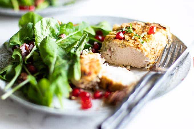 A piece of almond crusted chicken next to an arugula salad garnished with pomegranate seeds.