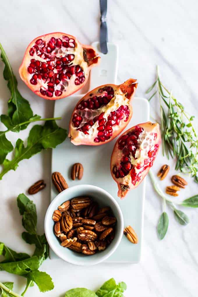 A blue cutting board with a pomegranate and some pecans on it.