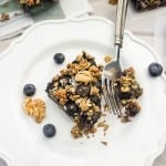 A blueberry oatmeal square on a white plate with a fork taking a bite.