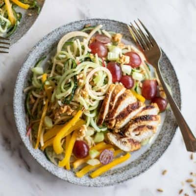 A plate showing a large salad with spiralized cucumber, apple, grilled chicken, grapes, peppers, and walnuts.