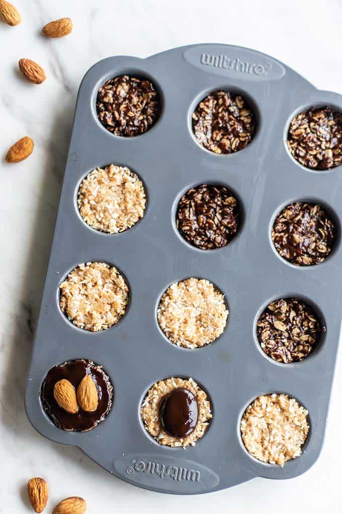 A mini muffin pan, showing how to layer the chocolate and coconut mixtures to make almond joy cookies.