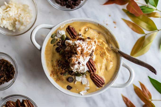 A festive fall smoothie bowl topped with whipped cream and pecans.