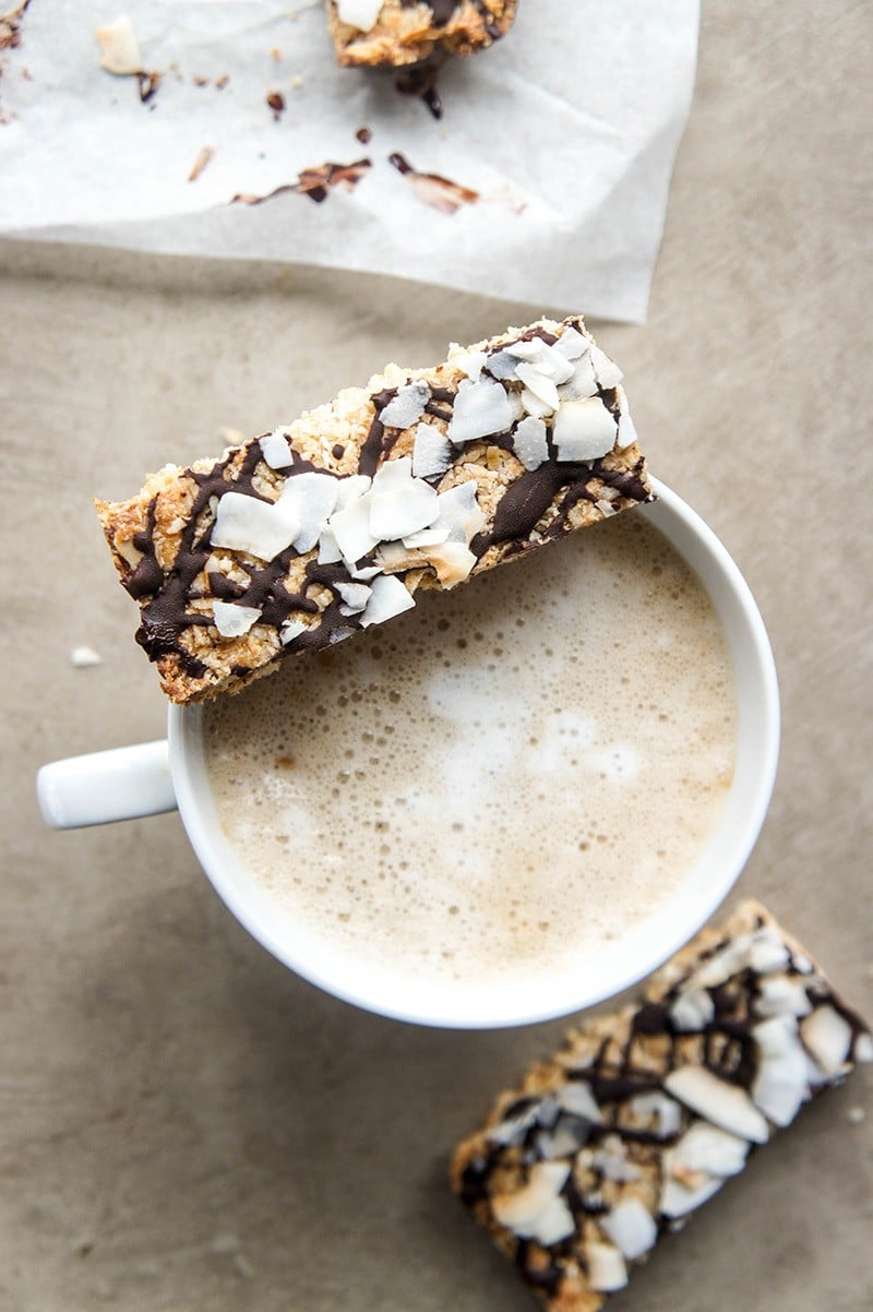 A homemade protein bar topped with drizzled chocolate and coconut flakes sitting on top a mug of coffee.