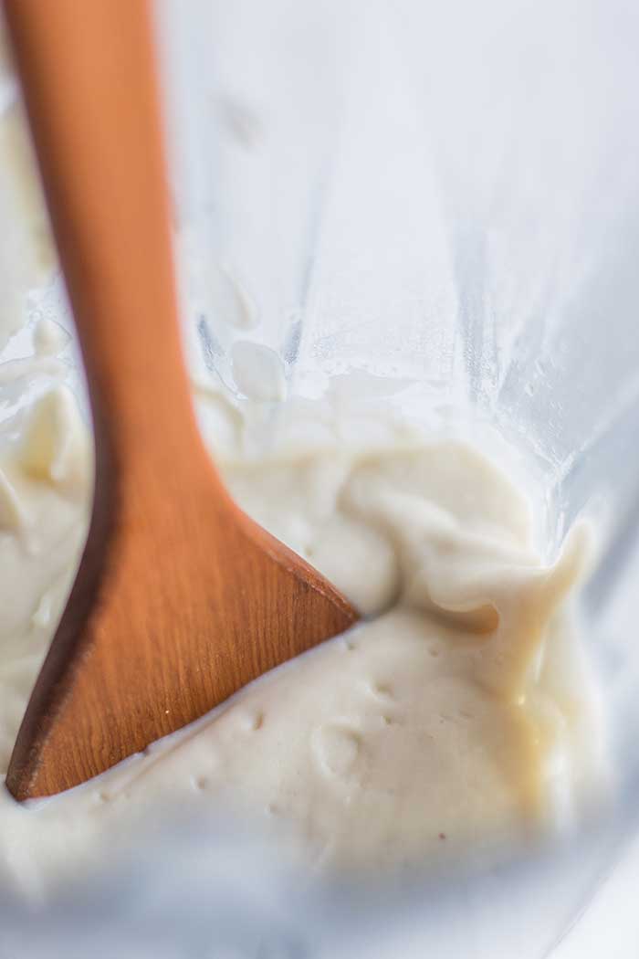 A wooden spoon dipping into a blender filled with a luxurious cashew cauliflower cream.