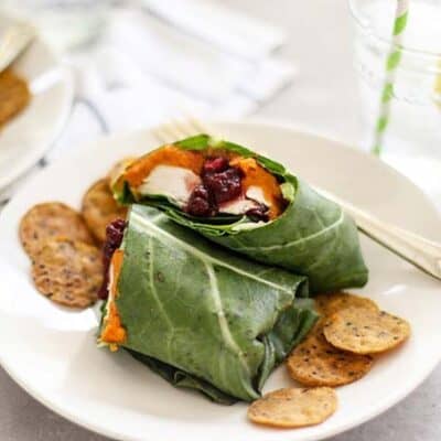 A white plate showing a collard wrap served with chips.