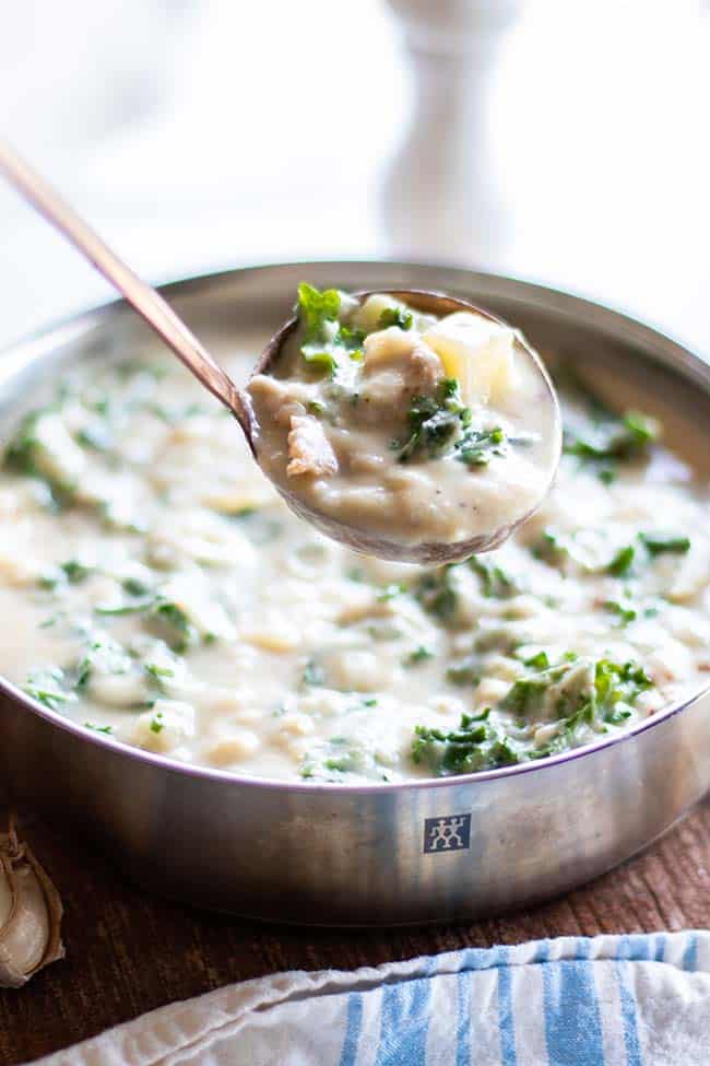 A pot of Zuppa Toscana with a ladle serving a scoop.