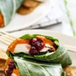 A close up of a plate with a turkey collard green wrap with sweet potato chips.