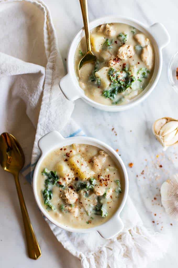 Two bowls of zuppa toscana garnished with red chili flakes.