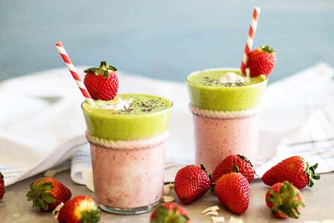 Two glasses layered with a pink and green strawberry colada smoothie.