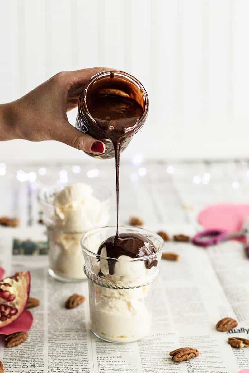 A far of hot fudge sauce being drizzled on a cup of ice cream.