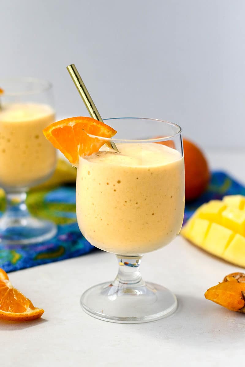 A gold turmeric smoothie in a glass garnished with an orange.