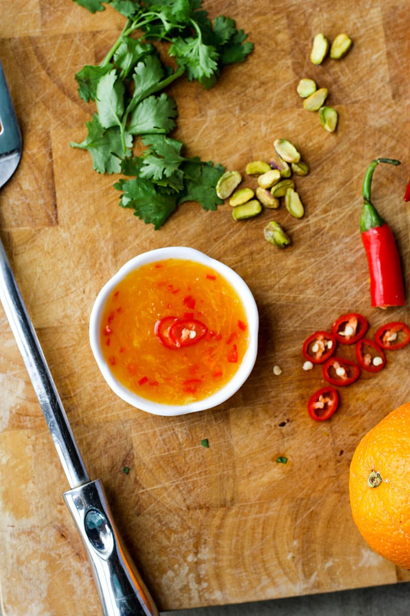 A cutting board with a ramekin of orange chili dipping sauce.