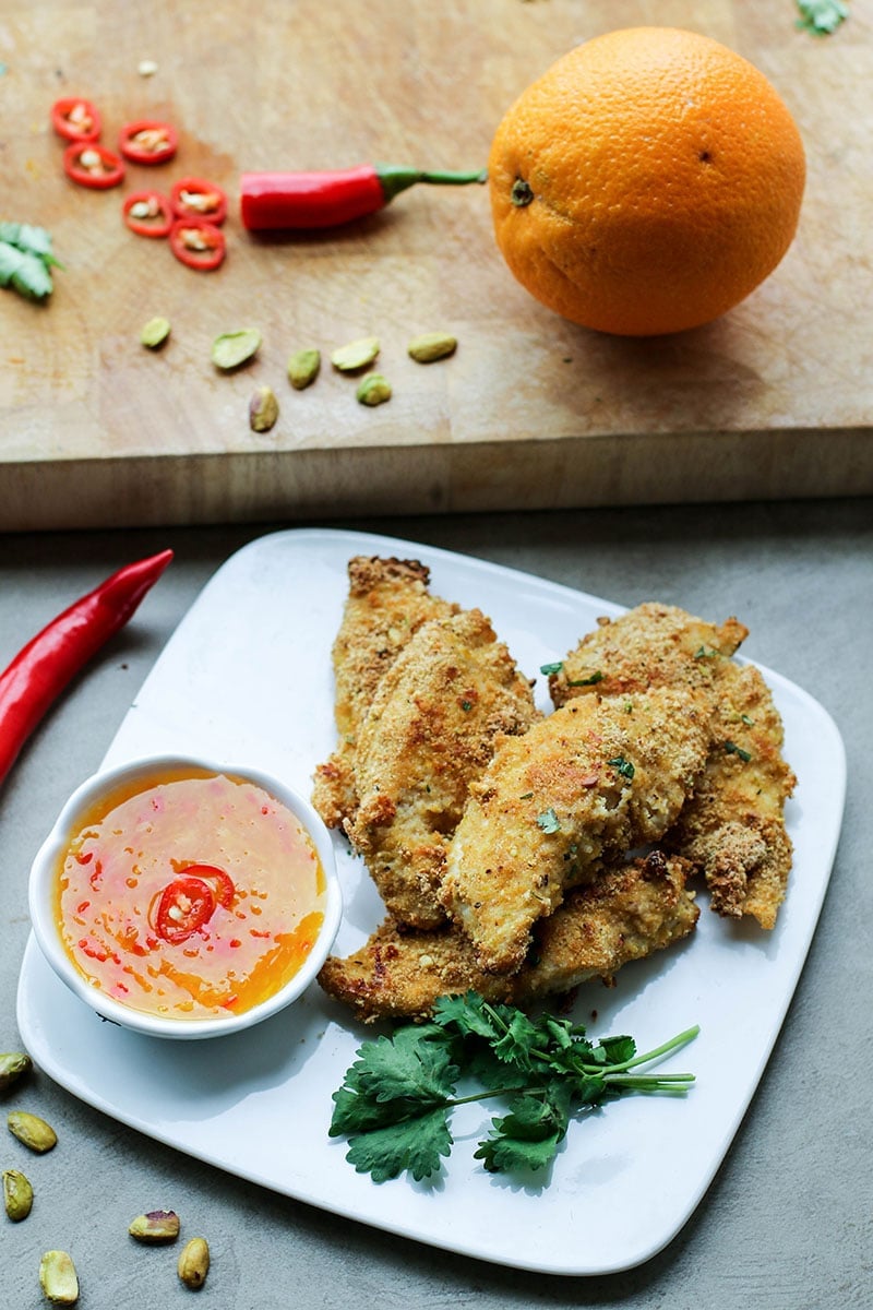 A plate of chicken fingers coated with pistachios served with an orange chili dipping sauce.