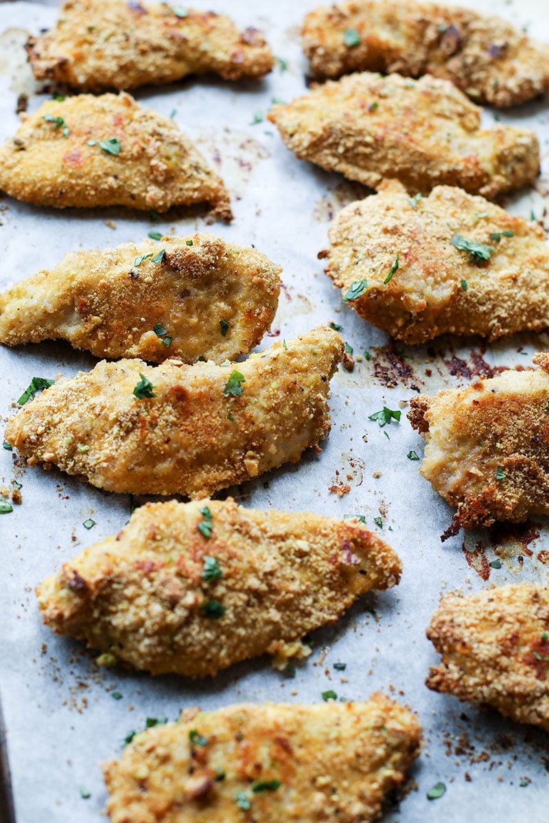 Golden brown baked chicken fingers on a baking tray, sprinkled with parsley.