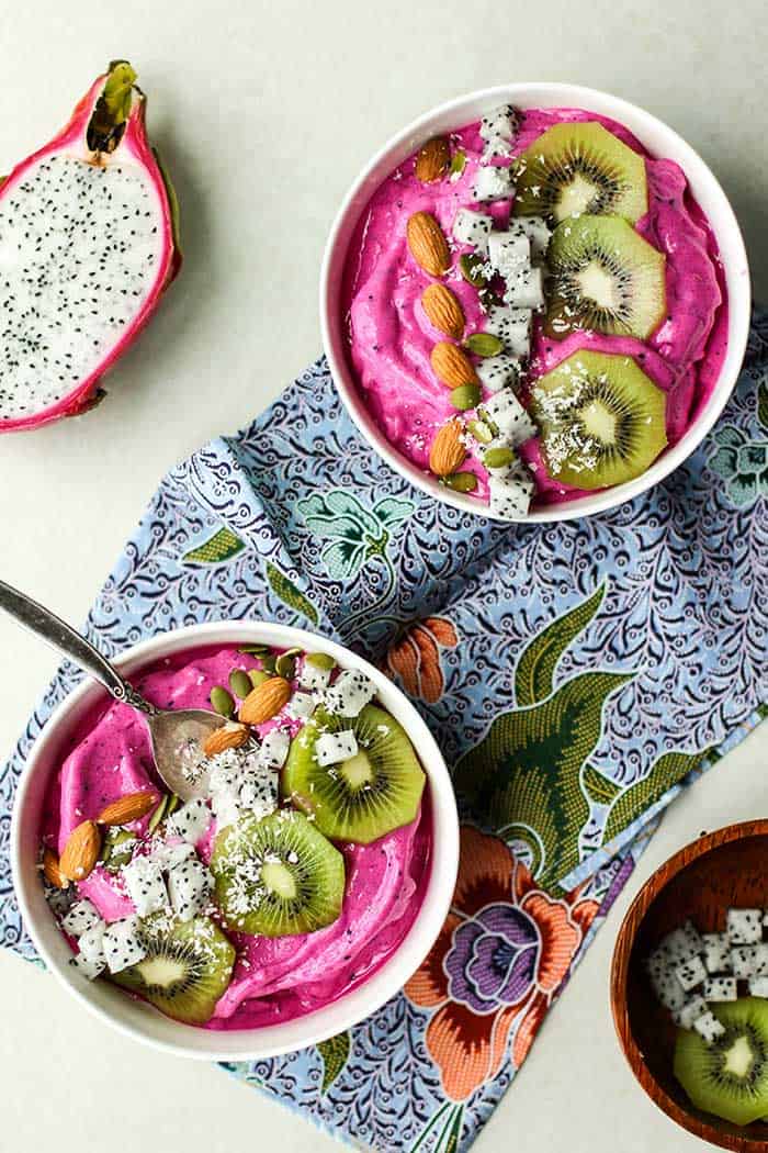 Two pitaya bowls and topped with kiwi, coconut and almonds.