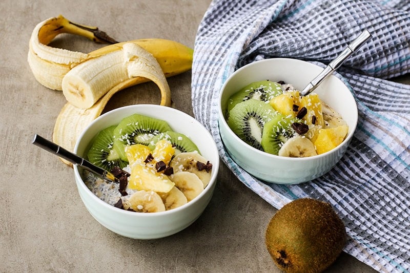 Two bowls of oats topped with pineapple, bananas, and kiwi.