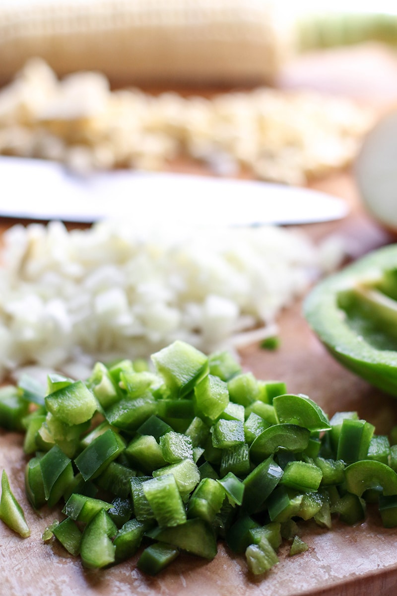 Chopped peppers, onions, and corn on a cutting board.