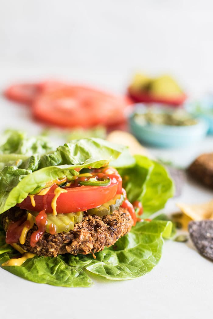 A pumpkin seed veggie burger wrapped in lettuce and topped with tomato and pickle.