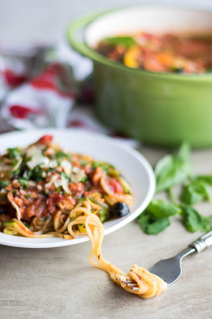 A plate of chicken vegetable spaghetti sauce, with zoodles spun around a fork.