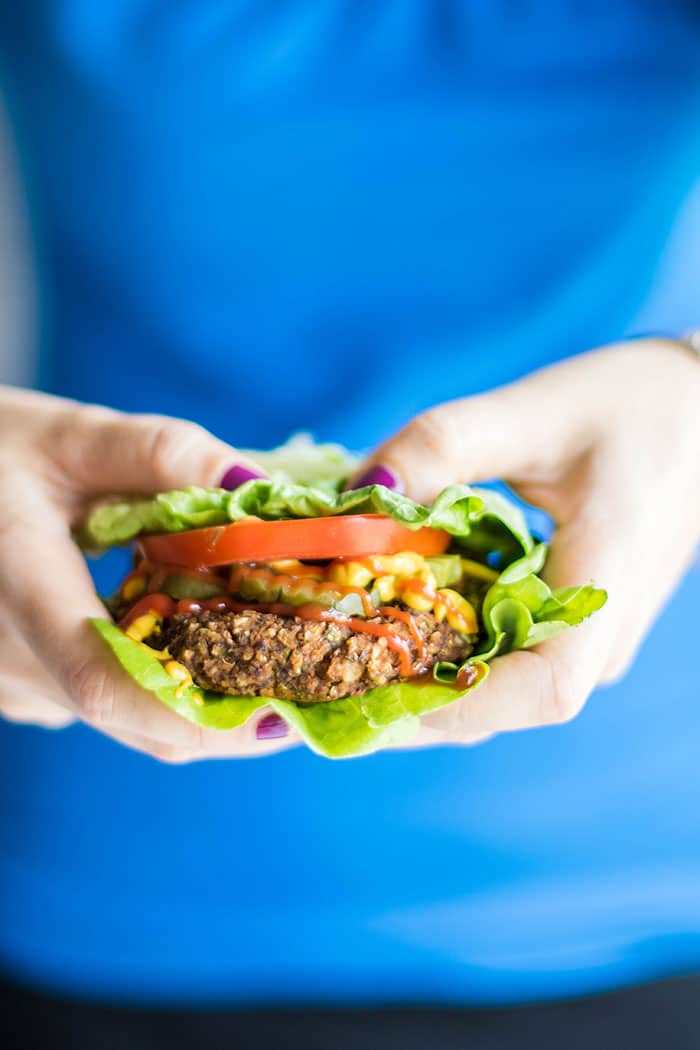 A pumpkin seed veggie burger wrapped in lettuce, held in hands.