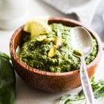 A bowl filled with pistachio pesto topped with lemon slices and pistachios.