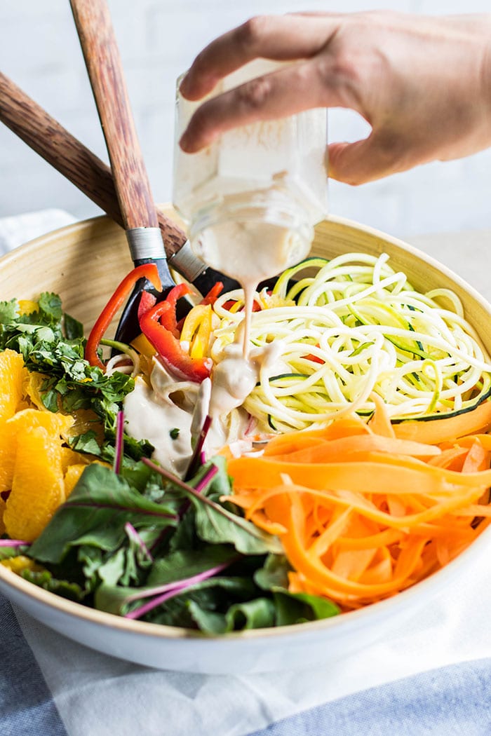 A colorful bowl of veggies being drizzled with a creamy tahini dressing.