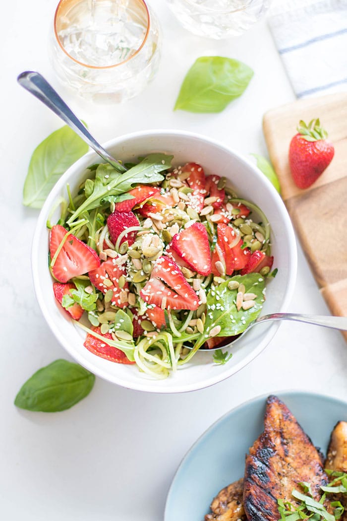 A bowl with a strawberry cucumber salad topped with sunflower and sesame seeds.