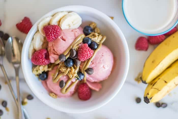 A healthy breakfast sundae in a white bowl with bananas on the side.
