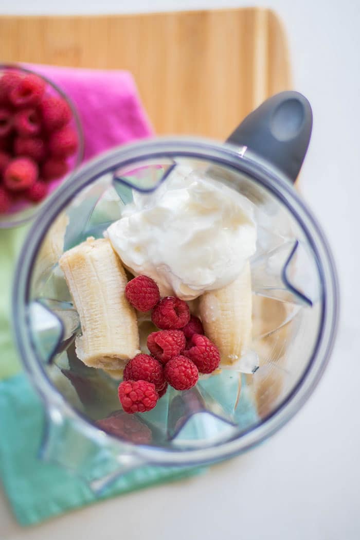 A blender filled with frozen bananas, raspberries, and plain yogurt.
